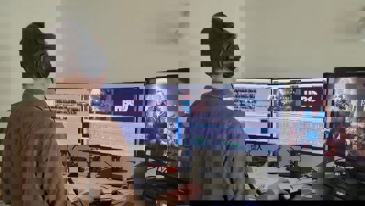 A person facing a set of computer monitors edits a sequence from a drama called The Regime.