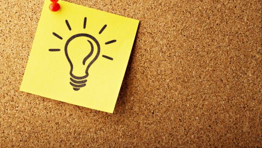 A Post-It note with a drawing of a lightbulb pinned to a cork board