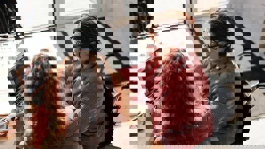 Two women, one in a wheelchair, sit at a desk looking at a laptop