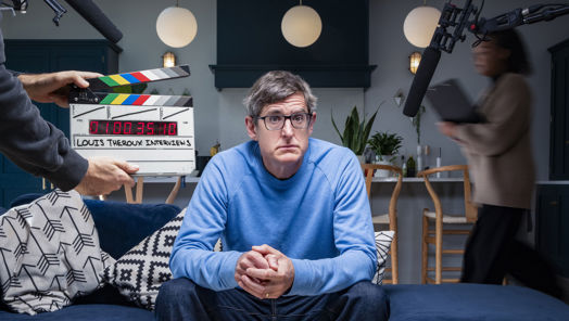 Louis Theroux sitting on a sofa in front of a clapper board