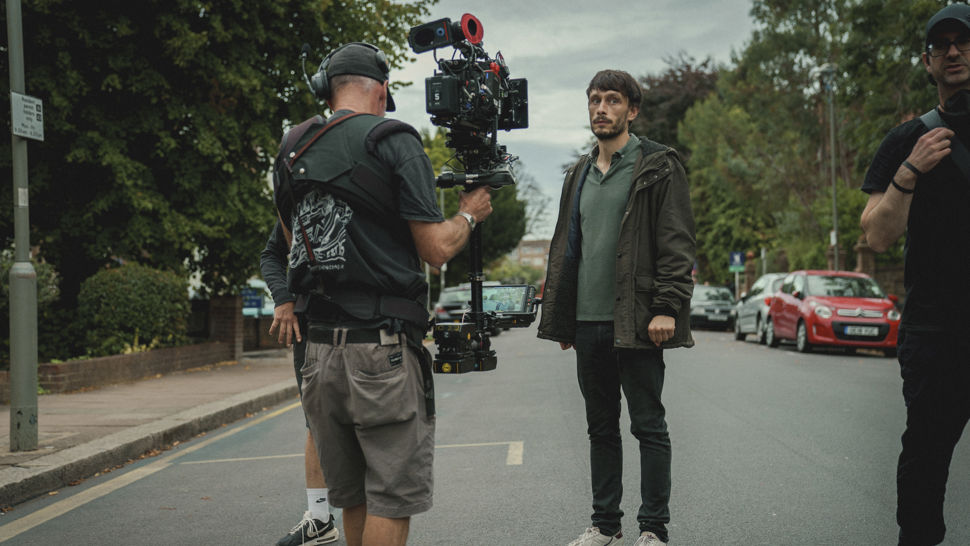 Behind-the-scenes image of Baby Reindeer creator and actor Richard Gadd as character Donny Dunn standing in the middle of a road in front of a cameraman