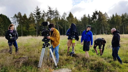 Camera crew standing in a grassy area 