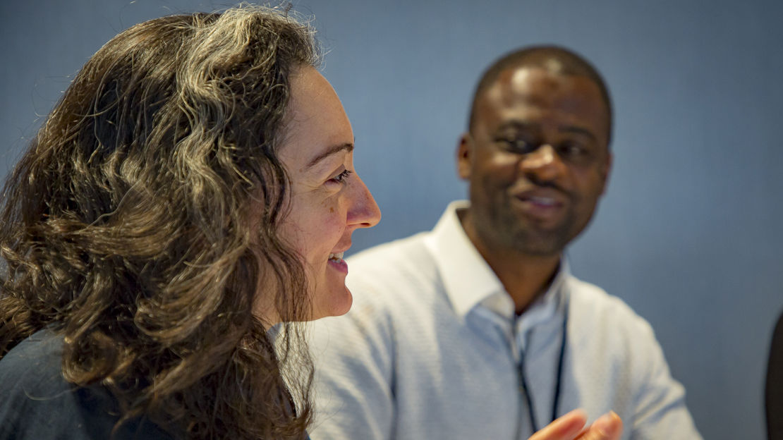 Woman in the foreground speaking and motioning with hands and a man in the background watching