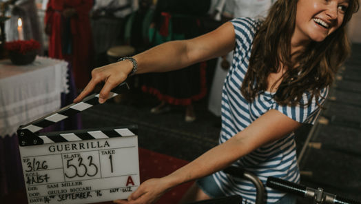 Behind-the-scenes image of a woman smiling while holding a clapper board on the set of the movie Guerilla