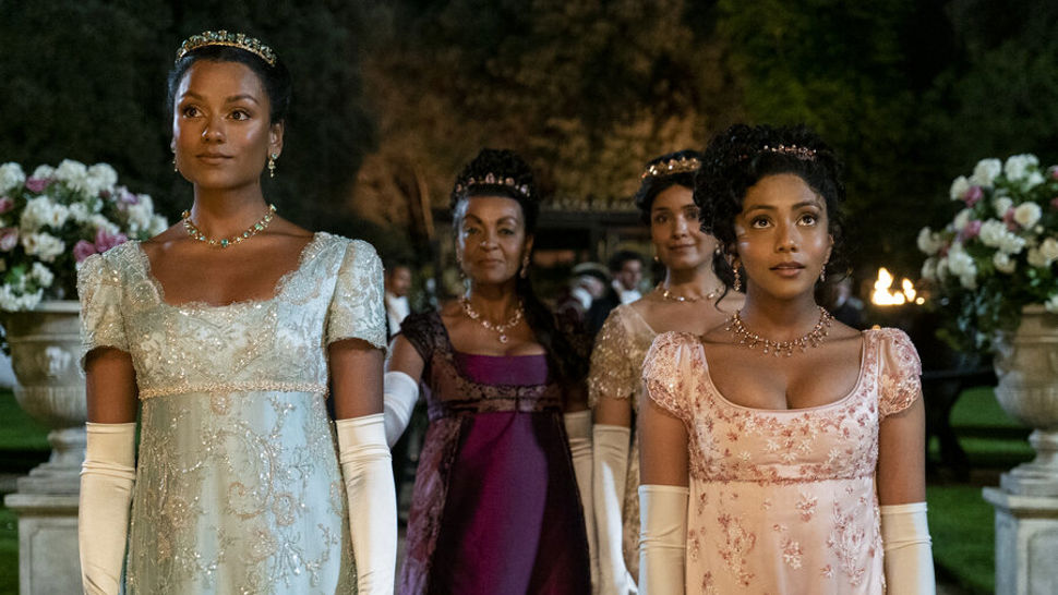 Image of actors Simone Ashley, Adjoa Andoh, Charithra Chandran and Shelley Conn wearing brightly coloured period dress walking through a garden of flowers in Bridgerton