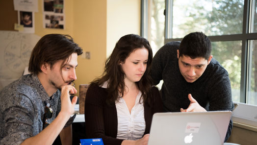Three young people gathered around a laptop on a desk
