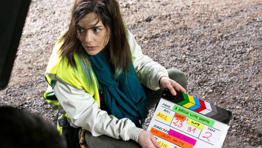 Woman crouching on the ground with a clapper board