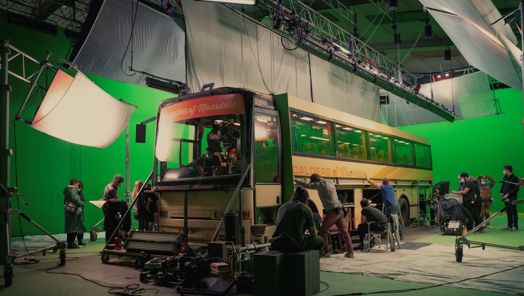 Behind-the-scenes of Sex Education season 3, production crew rig a large coach in front of a green screen with lights