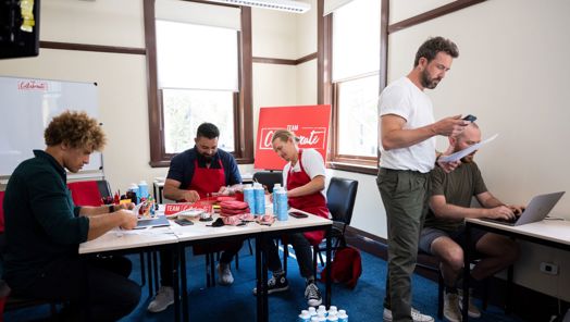 Several people sit around tables in a room working on a project