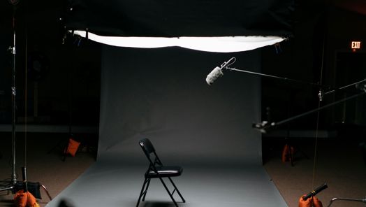 A fold up chair in the centre of a studio with a boom microphone pointing down from above
